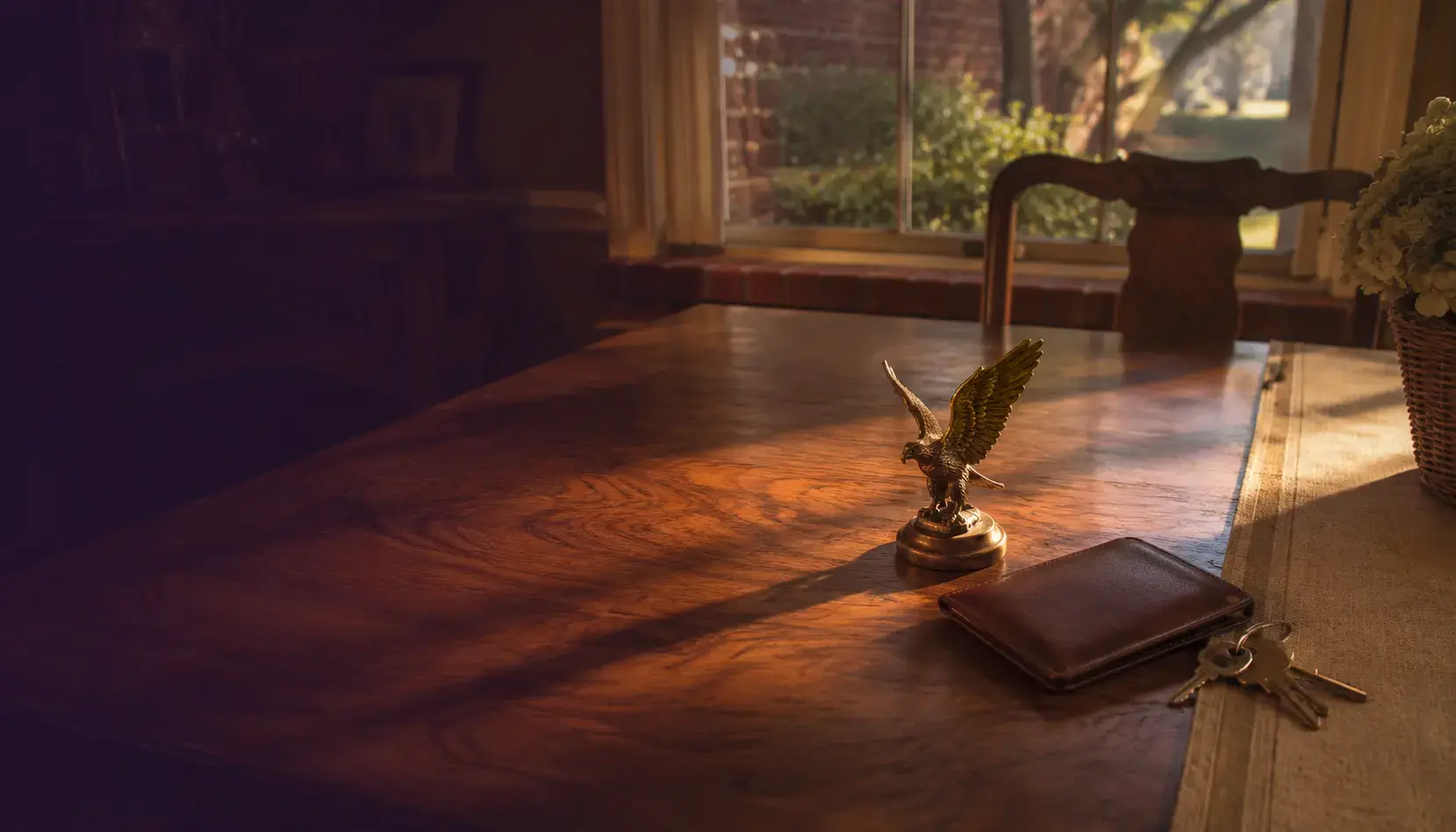 A small brass eagle paperweight beside a closed leather credentials wallet and house keys on a walnut table at golden hour