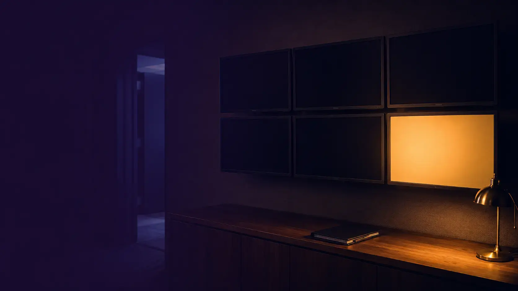 A dark office at night with a wall of six monitors, one glowing amber among five dark screens